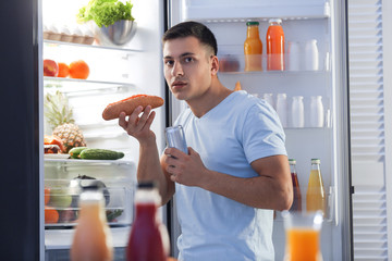 Afraid man caught in the act of eating unhealthy food near refrigerator at night