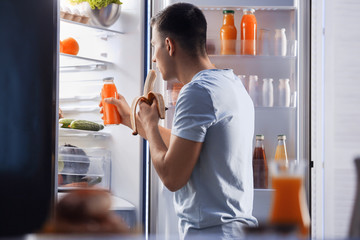 Handsome young man choosing food in refrigerator at night