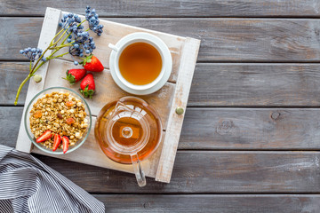 Breakfast in bed with granola, tea in pot and cup on tray on wooden background top view