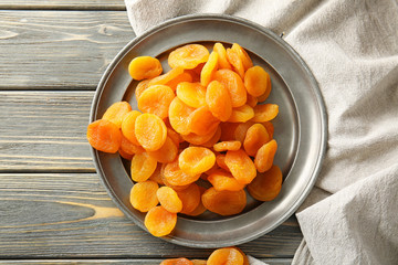 Plate with dried apricots on wooden background