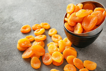 Bowl with dried apricots on grey background