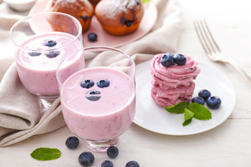 Glasses of tasty blueberry yogurt and marshmallow on white table