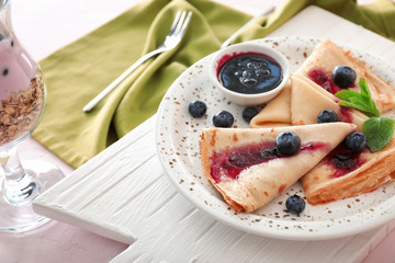 Plate with tasty blini and blueberry jam on table