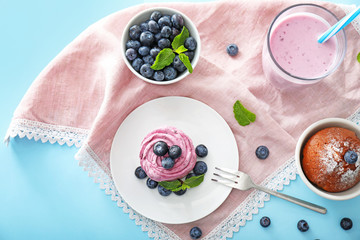 Tasty blueberry desserts with yogurt on color background