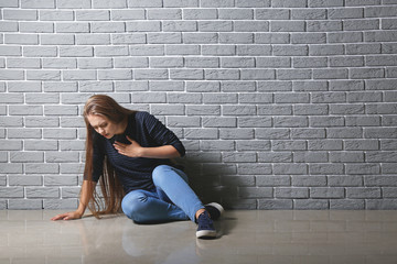 Fototapeta na wymiar Woman having panic attack while sitting near brick wall