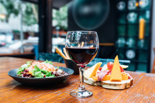 Dinner in the restaurant with Wine, Cheese and salad. Red wine glass, assorted cheese plate and smoked salmon salad on wooden dining table. This is Lunch or Dinner Restaurant or Cafe Concept Image.