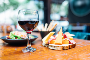 Dinner in the restaurant with Wine, Cheese and salad. Red wine glass, assorted cheese plate and smoked salmon salad on wooden dining table. This is Lunch or Dinner Restaurant or Cafe Concept Image.