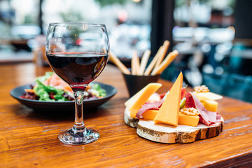 Dinner in the restaurant with Wine, Cheese and salad. Red wine glass, assorted cheese plate and smoked salmon salad on wooden dining table. This is Lunch or Dinner Restaurant or Cafe Concept Image.
