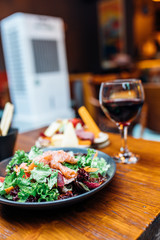 Dinner in the restaurant with Wine, Cheese and salad. Red wine glass, assorted cheese plate and smoked salmon salad on wooden dining table. This is Lunch or Dinner Restaurant or Cafe Concept Image.