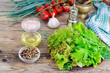 Green salad ingredients organic lettuce, cherry tomatoes, spices and olive oil on wooden background. 