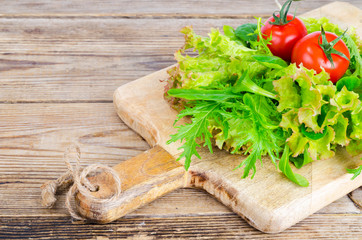 Green salad ingredients organic lettuce, cherry tomatoes, spices and olive oil on wooden background. 