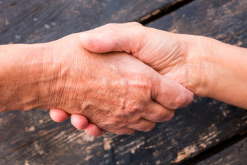 Two shaking hands. Love and friendship concept. Aid for old people. Trust and security for elderly. Caucasian human hands on black wooden background