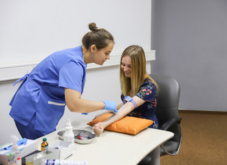 Doctor Injecting patient in arm With Syringe To Collect Blood. Nurse pierce arm vein of a young woman for blood donation/Doctor makes the patient an injection into a vein