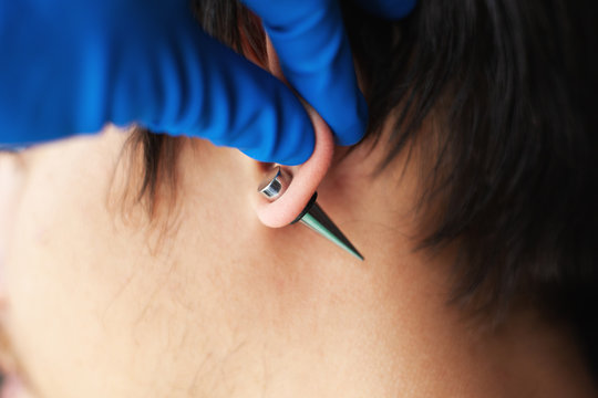stretching ears for larger diameter tunnels,piercer hand inserts the piercing in the ear