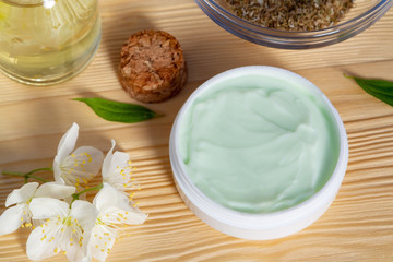 Jar of cream made from natural plant ingredients, oils and herbs, jasmine flowers on a light wooden background - preparation of organic cosmetics concept, close up