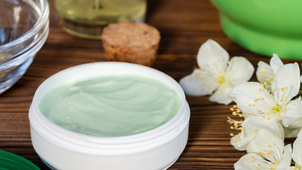 Jar of cream made from natural plant ingredients, oils and herbs, jasmine flowers on a dark wooden background - preparation of organic cosmetics concept, close up