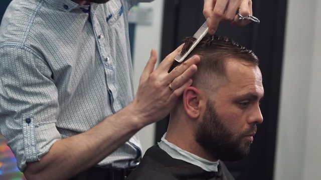Close up shot of man getting trendy haircut at barber shop. Male hairstylist serving client, making haircut using machine and comb