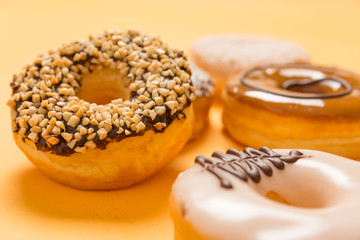 A variety of flavoured doughnuts on yellow background close up food concept image.