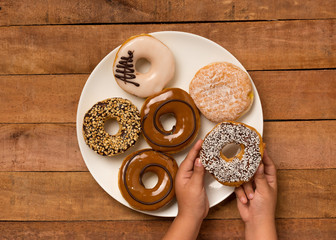 A young girl picking up a doughnut off plate.