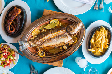 Turkish or Greek restaurant table and food dinner cuisine culture from top view. Traditional Greek ouzo or turkish raki with grilled or fried fish and appetizers on dinner table at restaurant. 