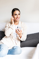 Smiling woman wearing earbeans, using laptop at home, sitting on sofa in living room