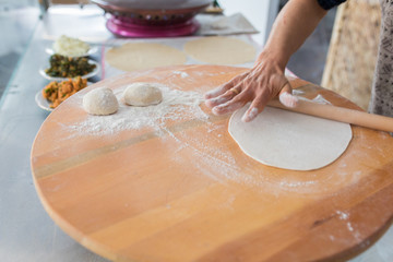 Woman preparing or making borek or bread dough. Hands keep rolling pin on dough with flour. Borek, bread or pastry dough on a wooden table background. Traditional Turkish pide, pita or yufka bread.