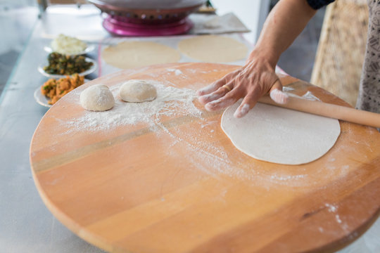 Woman preparing or making borek or bread dough. Hands keep rolling pin on dough with flour. Borek, bread or pastry dough on a wooden table background. Traditional Turkish pide, pita or yufka bread.