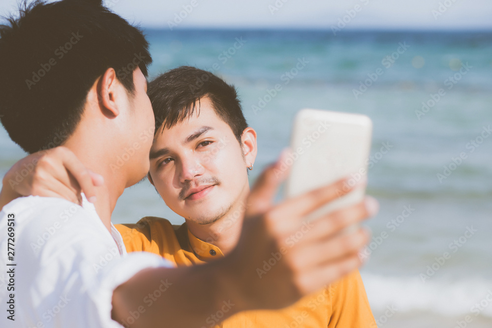 Wall mural gay portrait young couple smiling taking a selfie photo together with smart mobile phone at beach, l