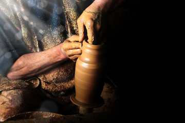 Close up mud covered hands of adult man making clay pot on potter's wheel