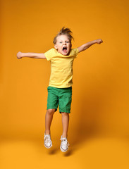 Fototapeta na wymiar Full length portrait of an excited young boy jumping leaping in green shorts over yellow 