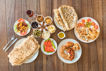 Traditional Turkish Breakfast Table. Turkish Breakfast Food Cuisine Culture. Turkish pide yufka ekmek, tea, bagel, borek, sikma, cheese, olives, oil and honey on wooden table from top view.