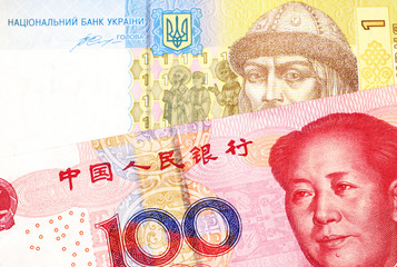 A close up image of a red, Chinese one hundred yuan note with a yellow and blue Ukrainian A Ukrainian one hryvnia bill close up in macro