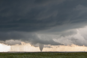 Obraz na płótnie Canvas A cone tornado touches down under the base of a dark storm on the plains in Wyoming.