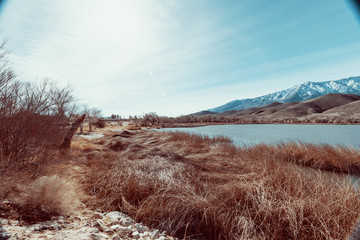 a lake in front of the snow-covered mountains of Alabama hills. Dry grass in the foreground. 