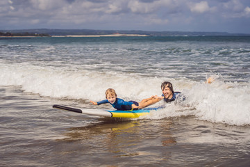 Father or instructor teaching his 5 year old son how to surf in the sea on vacation or holiday. Travel and sports with children concept. Surfing lesson for kids