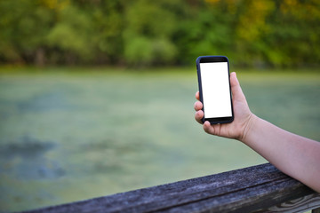 woman's hand holding cell phone in front of scummy pond - screen white out - horizontal