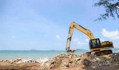 excavator digger stone working on construction site - backhoe loader on the beach sea ocean and blue sky background