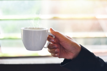 White coffee cup in hand , close up - Business woman holding coffee cup by the window with sunlight in the morning