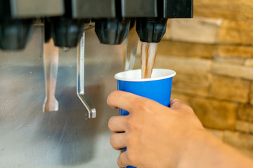 hand holding a paper glass to pour the lemonade soda soft drink  machine  in a fastfood restaurant