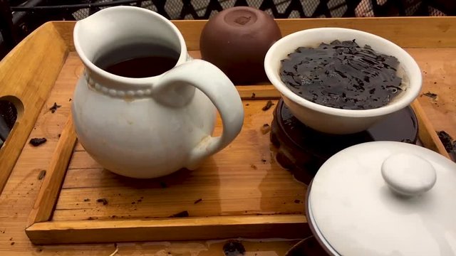 A close up shot of a Chinese tea session made with whole leaf Pu-Erh tea in a Gaiwan set on a bamboo tea tray.