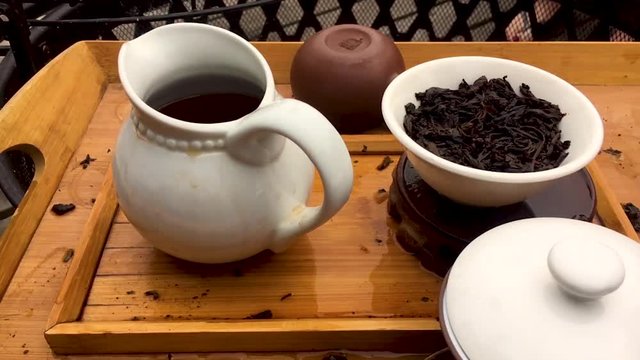 A close up shot of a Chinese tea session made with whole leaf Pu-Erh tea in a Gaiwan set on a bamboo tea tray.