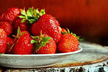 full plate with sweet natural big rustic red ripe strawberries on split sawn birch stump on aged wooden background close up