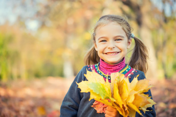 Portrait of happy little girl with autumn leaves in the park