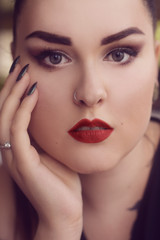 Portrait of a girl with professional make-up,.smoky eyes, red lips and smooth eyebrows. Limbed eyebrows. Girl with piercing in the nose. Piercing, rings. Brunette with long nails, manicure.