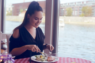 Brunette girl with a tail sitting in a restaurant on ship on the background of the river. Girl tries salmon with rice. Girl eats appliances. Woman with the tunnels in the ears and piercing in the nose