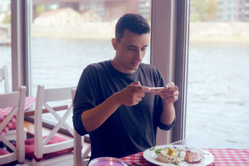 Male food blogger takes a picture on the phone from social networks. A man shooting food in a restaurant. A man makes a photo of salmon and risotto, dish. National food, tourist smile. Roaming.