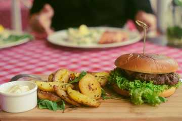 Meat burger with fries, mayonnaise potatoes on a wooden board. Restaurant dish. Food in the cafe, eatery. Fast food. A fat dish. burger with meat and lettuce. Board on the tablecloth in the cell