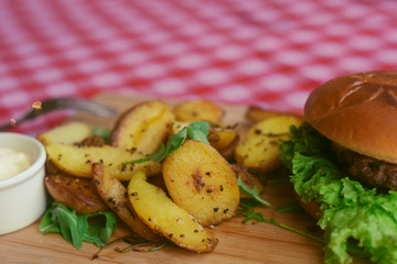 Meat burger with fries, mayonnaise potatoes on a wooden board. Restaurant dish. Food in the cafe, eatery. Fast food. A fat dish. burger with meat and lettuce. Board on the tablecloth in the cell