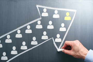 Leadership and teamwork concept. Businessman drawing arrow and team on chalkboard.