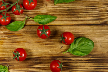 Fresh cherry tomatoes with green basil leaves on a wooden table. Top view
